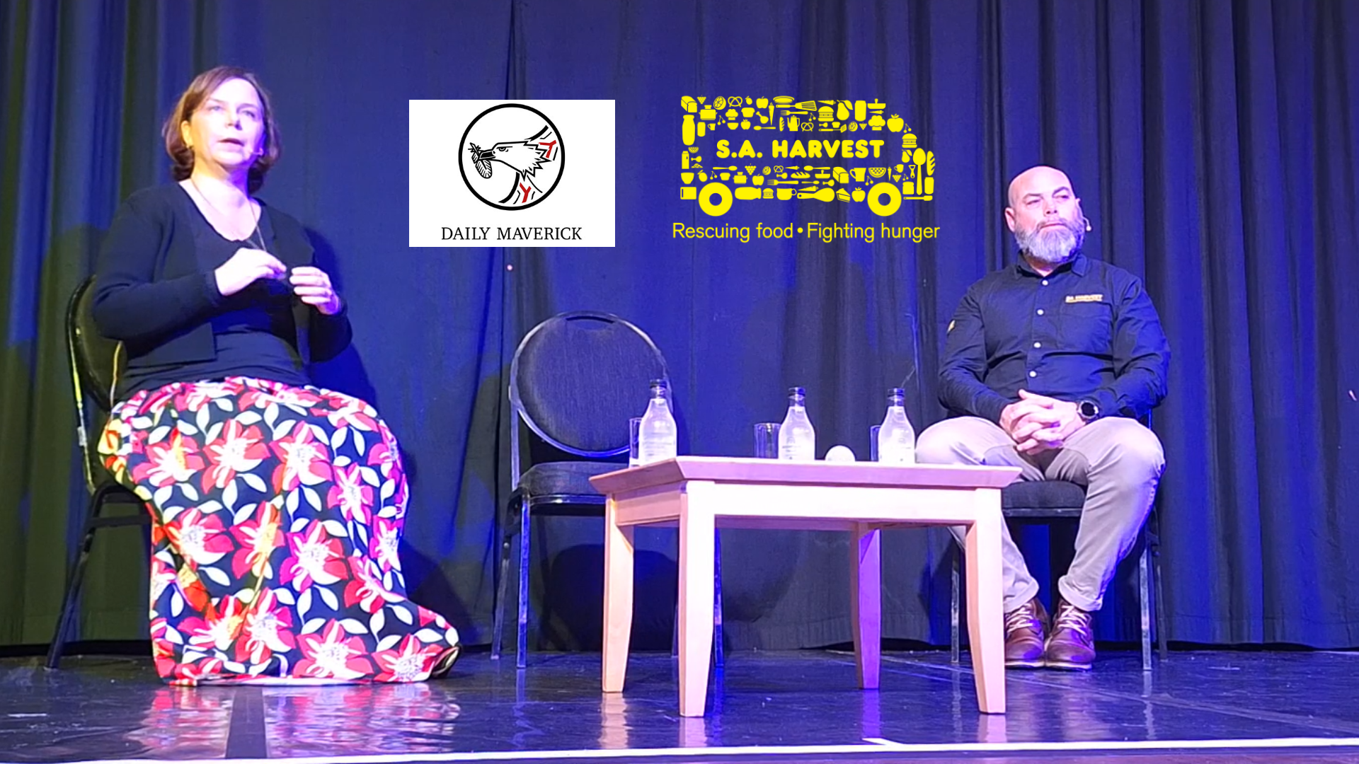 Estelle Ellis and Ozzy Nel seated on stage at the Hermanus FynArts Festival for the Daily Maverick WAKE UP session titled “The Impact of Ordinary People,” with Daily Maverick and SA Harvest logos visible behind them.